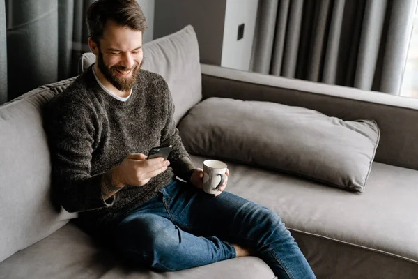 Hombre Barbudo Usando Teléfono Móvil Tomando Café Mientras Está Sentado — Foto de Stock