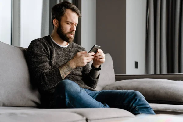 Barbudo Hombre Europeo Usando Teléfono Móvil Mientras Está Sentado Sofá — Foto de Stock