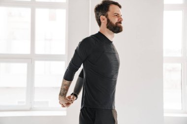 Sakin, orta yaşlı, sakallı, spor kıyafetli bir adam pencerenin yanındaki odada ellerini uzatıyor.