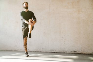 Orta yaşlı, sakallı, beyaz bir adam stüdyoda bacaklarını açıyor.