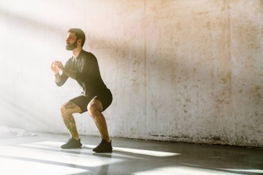 Orta yaşlı beyaz sakallı adam içeride egzersiz yapıyor.