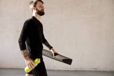 Orta yaşlı, sakallı beyaz adam elinde su şişesi ve spor paspası tutuyordu.