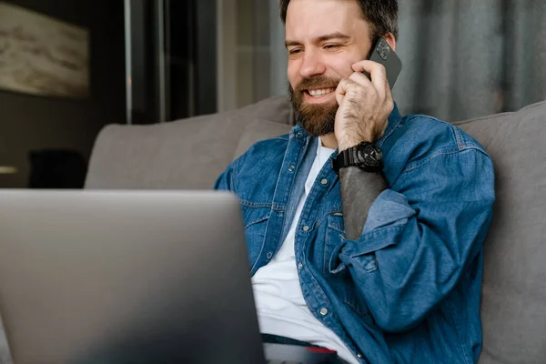 Homem Barbudo Falando Telefone Celular Enquanto Trabalhava Com Laptop Sofá — Fotografia de Stock