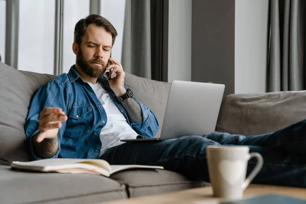 Бородатий Чоловік Розмовляє Мобільному Телефоні Використовує Ноутбук Під Час Роботи — стокове фото
