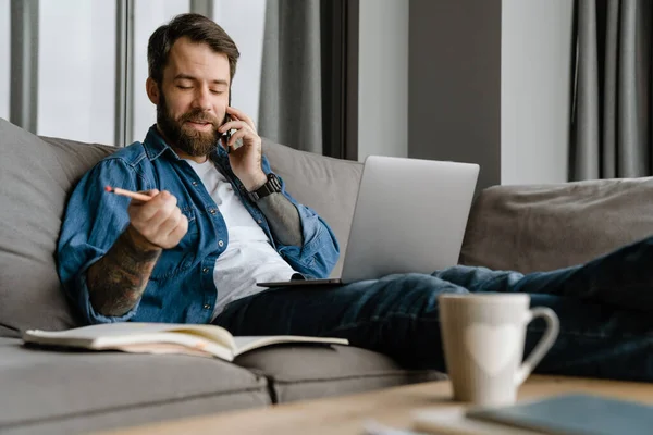 Бородатий Чоловік Розмовляє Мобільному Телефоні Використовує Ноутбук Під Час Роботи — стокове фото