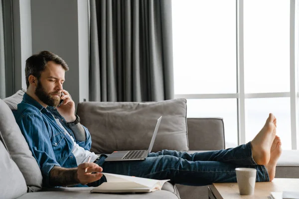 Bearded Man Talking Cellphone Using Laptop While Working Home — Stock Photo, Image