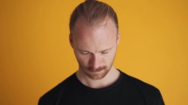 Gülümseyen adam sarı stüdyodaki kameraya bakıyor.