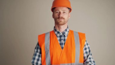 Konsantre müteahhit gri stüdyodaki kameraya bakıyor.