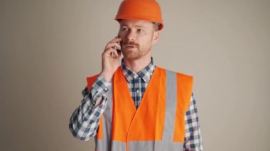 Gri stüdyoda telefonla konuşan kendine güvenen bir müteahhit.