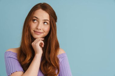 Mavi duvarın arkasında duran, uzun kızıl saçlı, gülümseyen, sıradan bir kadının portresi.