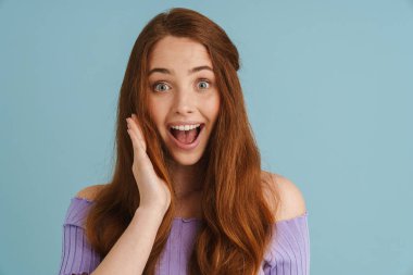 Genç kızıl, mavi arka planda mahsur kalmış kamera karşısında şaşırdığını ifade eden heyecanlı bir kadın.