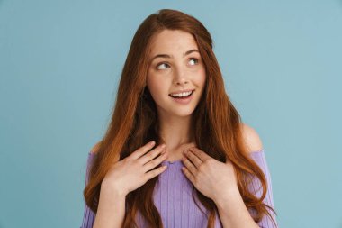 Genç kızıl kadın gülümsüyor ve elini göğsüne koyuyor mavi arka planda izole bir şekilde.