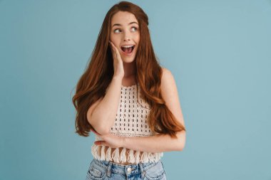 Genç kızıl, mavi arka planda mahsur kalmış kamera karşısında şaşırdığını ifade eden heyecanlı bir kadın.