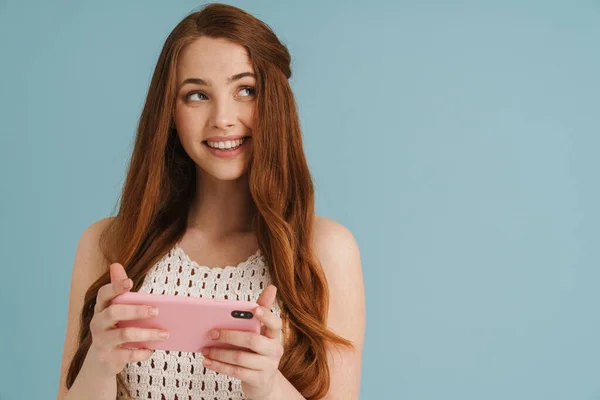 Молодая Рыжая Женщина Улыбается Используя Мобильный Телефон Изолирован Синем Фоне — стоковое фото