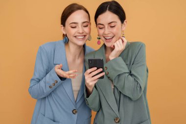 Sarı arka planda izole edilmiş cep telefonu kullanan iki genç kadın.