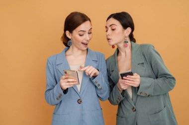 Sarı arka planda izole edilmiş cep telefonunu kullanan ve işaret eden iki genç kadın.