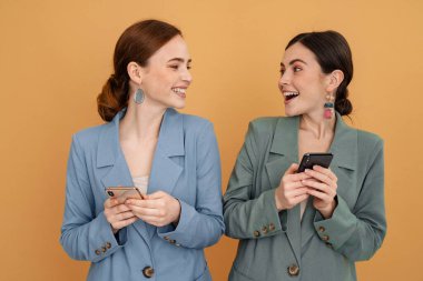 Sarı arka planda izole edilmiş cep telefonlarıyla gülen iki genç kadın.