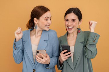 İki genç kadın cep telefonu kullanıyor ve kazanan hareketi sarı arka planda izole ediyor.