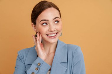 Sarı arka planda yalnız kalmış, gülümseyen ve yan bakan ceketli genç kızıl kadın.