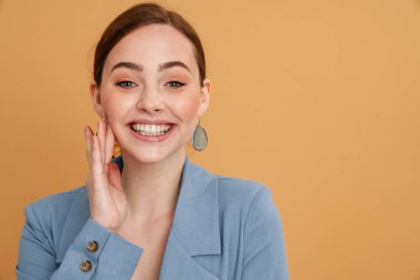 Ceketli genç kızıl kadın gülümsüyor ve sarı arka planda izole edilmiş kameraya bakıyor.