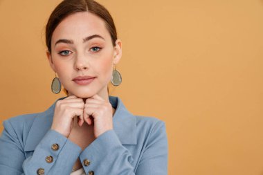 Ceketli genç kızıl kadın sarı arka planda yalnız poz veriyor ve kameraya bakıyor.