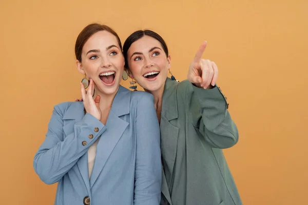 Молодые Две Женщины Куртках Улыбаясь Указывая Пальцем Вверх Изолированы Желтом — стоковое фото