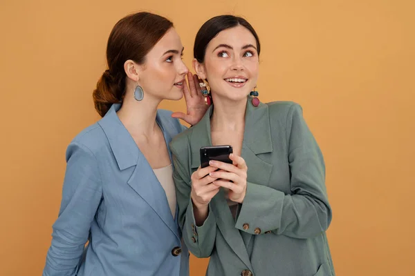 Mladé Dvě Ženy Šeptání Při Použití Mobilního Telefonu Izolované Přes — Stock fotografie