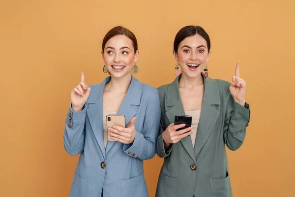 Mladé Dvě Ženy Pomocí Mobilních Telefonů Ukazuje Prsty Nahoru Izolované — Stock fotografie