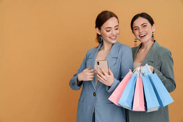 Jovens Duas Mulheres Segurando Sacos Compras Usando Celular Isolado Sobre — Fotografia de Stock