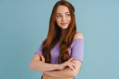 Mavi duvarın arkasında duran, kollarını kavuşturmuş, gülümseyen, kızıl saçlı, sıradan bir kadının portresini yakından çek.