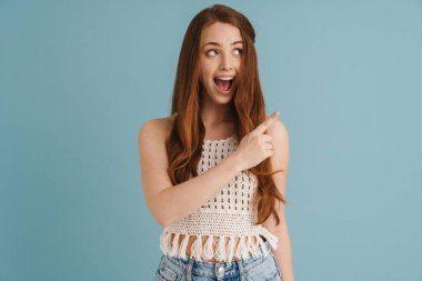 Genç kızıl, heyecanlı bir kadın. Mavi arka planda tek başına parmak sallıyor ve işaret ediyor.