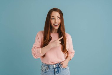 Genç kızıl kadın gülümseyip işaret ediyor mavi arka planda soyutlanmış bir şekilde.