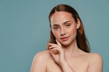 Mavi arka planda yarı çıplak kızıl kadın poz veriyor ve kameraya bakıyor.