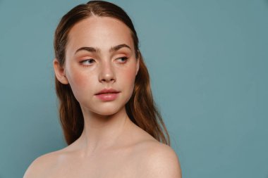 Mavi arka planda yarı çıplak kızıl kadın poz veriyor ve bir kenara bakıyor.