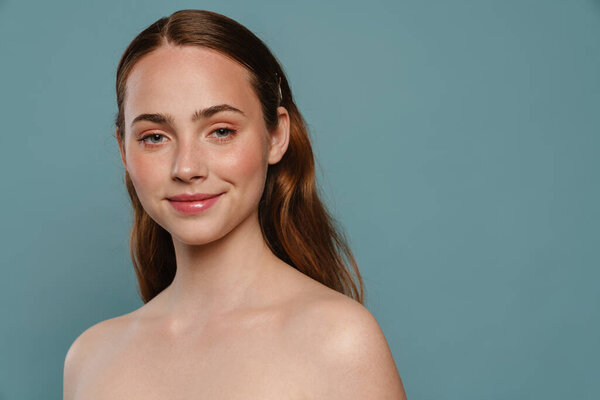 Half-naked ginger woman smiling and looking at camera isolated over blue background