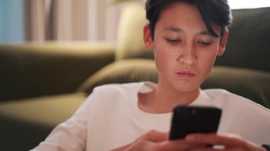 Kanepede telefonla mesajlaşan kendine güvenen esmer Asyalı adam.