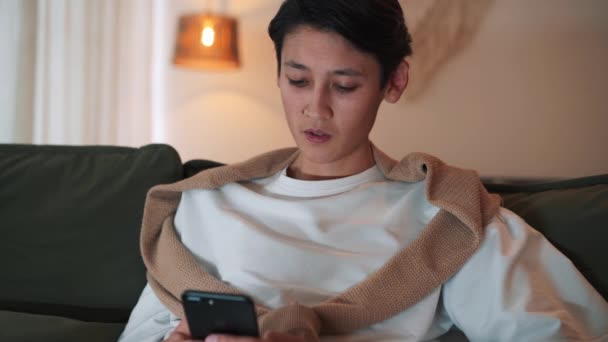 Concentrado Asiático Hombre Mensajes Texto Por Teléfono Mirando Televisión Casa — Vídeos de Stock