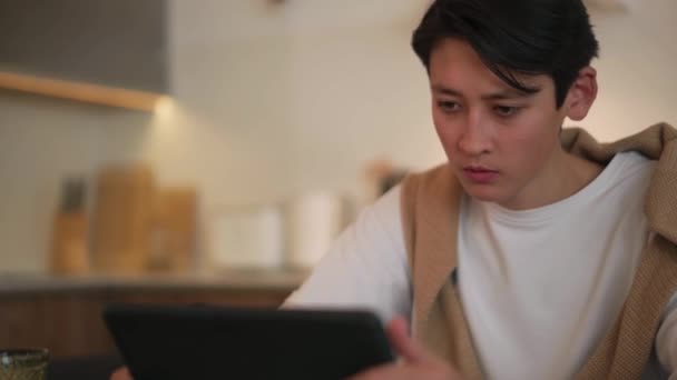 Ontevreden Aziatische Man Zoek Naar Tablet Sms Telefoon Thuis — Stockvideo