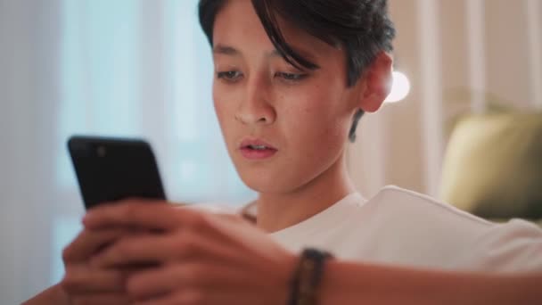 Pensive Brünett Asiatisch Mann Texting Telefon Auf Die Sofa — Stockvideo