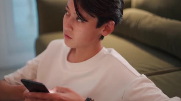 Serious Brünett Asiatisch Mann Texting Telefon Auf Die Sofa — Stockvideo