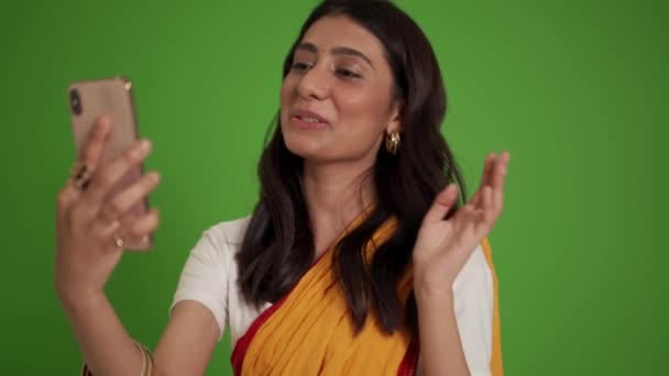 笑顔伝統的なインドの女性のビデオ通話で電話で緑のスタジオ — ストック動画