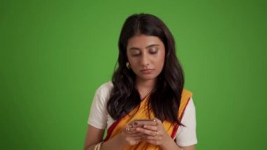 Düşünceli geleneksel Hintli kadın yeşil stüdyoda telefonla mesajlaşıyor.