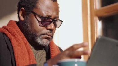 Gözlüklü gülümseyen Afrikalı adam açık kafede tablete bakıyor.