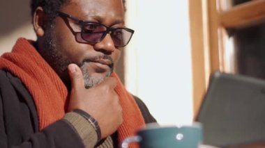 Dışarıdaki kafede gözlüklü bir Afrikalı adam tablete bakıyor.