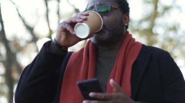 Gülümseyen Afrikalı adam parkta kahve içiyor.