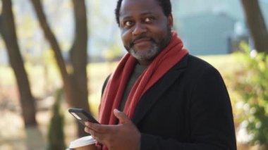 Gülümseyen Afrikalı adam parktaki telefona bakıyor.