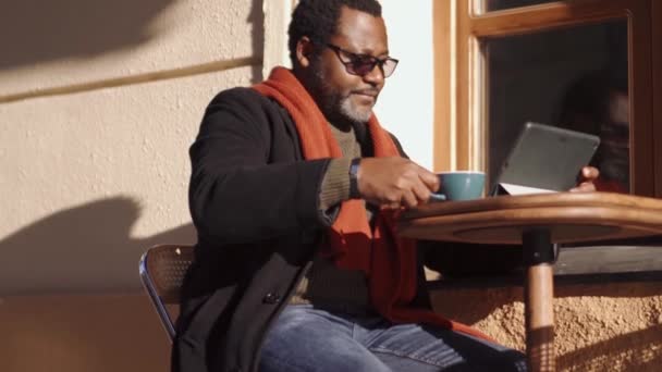 Positiver Afrikaner Mit Brille Blättert Mit Tablet Band Und Trinkt — Stockvideo