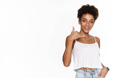 Young black woman in tank top smiling and gesturing at camera isolated over white background