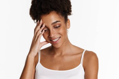 Young black woman in tank top smiling and covering her face isolated over white background