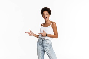 Young black surprised woman in tank top pointing fingers aside isolated over white background